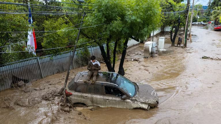 Una persona sentada sobre el techo de un auto rodeado de barro en una calle de Las Condes