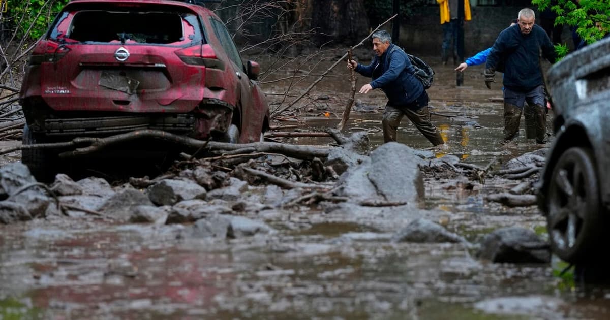 Dos hombres avanzan entre el barro y las piedras junto a un auto dañado tras el aluvión en Las Condes