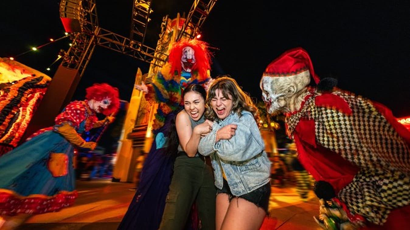 Dos visitantes gritan rodeadas de actores disfrazados de payasos en un evento nocturno de terror