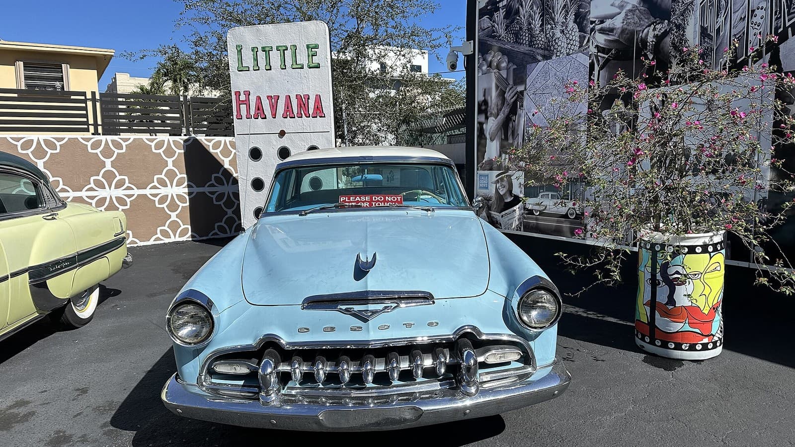 Un cartel con forma de ficha de dominó que dice Little Havana, junto a un auto antiguo en la Calle Ocho