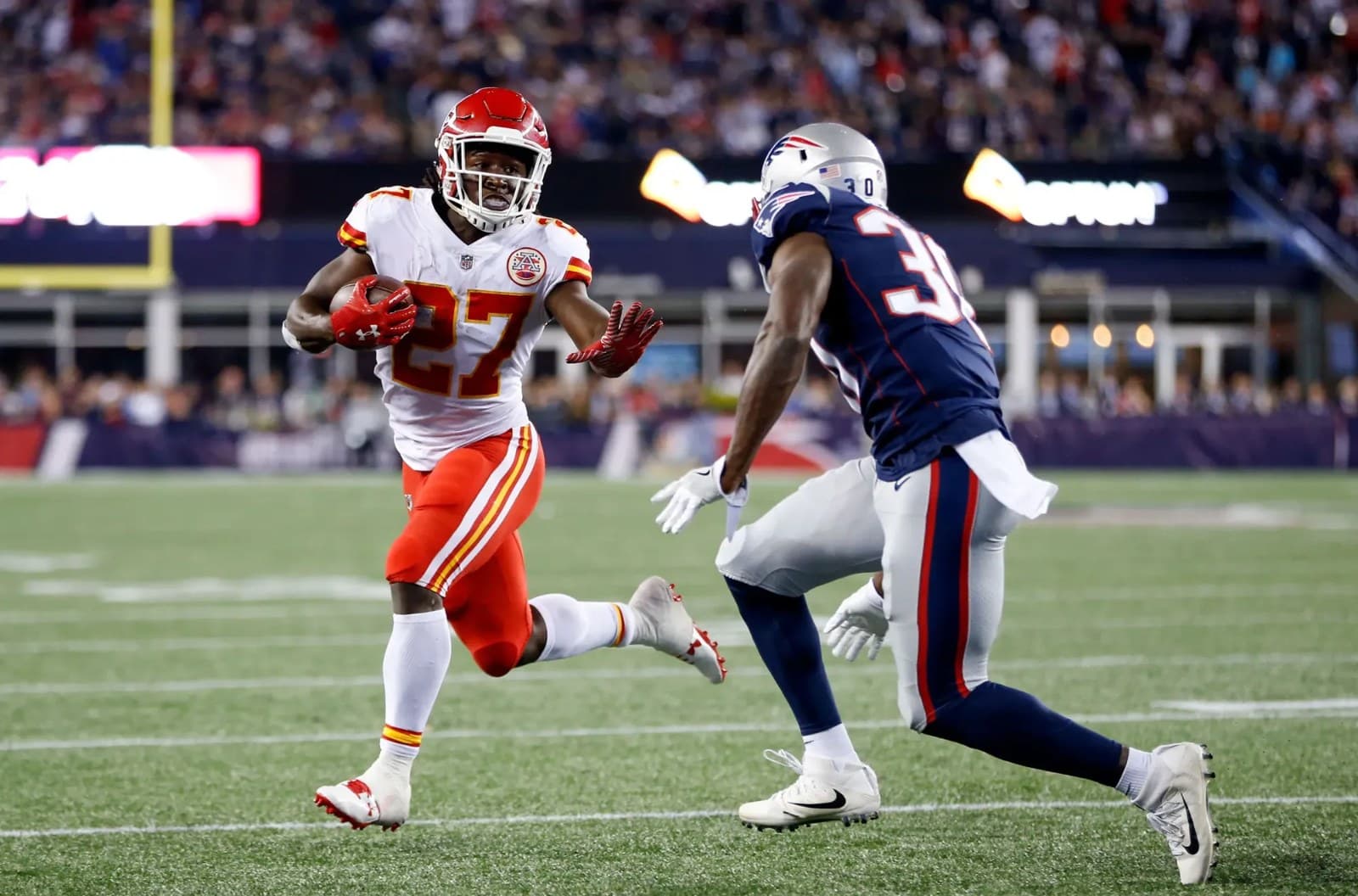 Un corredor de los Kansas City Chiefs avanza con el balón frente a un defensor de los New England Patriots